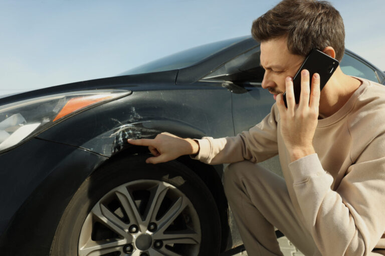 Man talking on phone near car with scratch outdoors